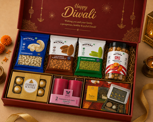 A Diwali gift hamper box filled with assorted snacks and treats, including Nutra brand packaged nuts and seeds, Ferrero Rocher chocolates, pink candles, and a small boxed item, arranged inside an open red gift box with Diwali-themed gold print and a 'Happy Diwali' message.